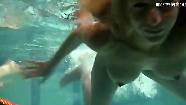 Two naked beauties swim in the pool